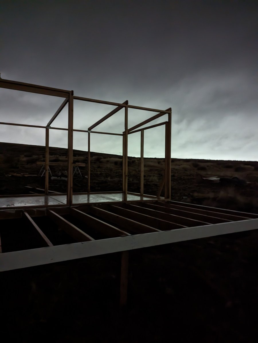 Bare timber frame on a raised platform against a stormy dusk sky on the sagebrush steppe