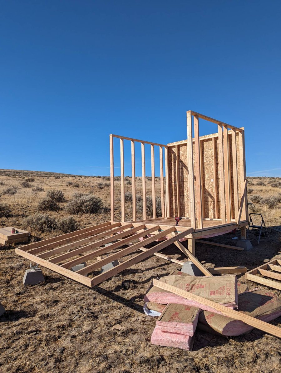 Framed and sheathed walls going up on pier blocks, with insulation staged in the foreground