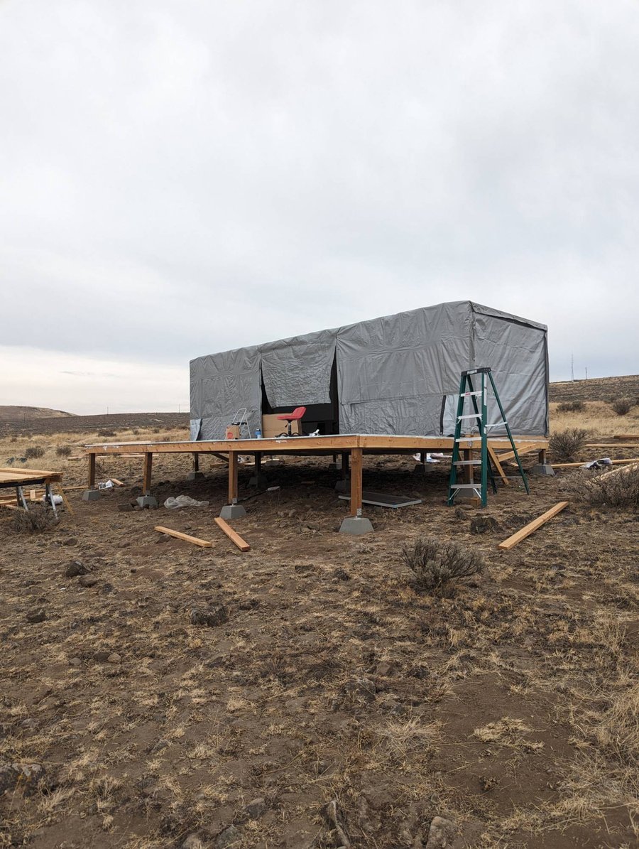The structure tarped weathertight on its raised platform, workspace inside